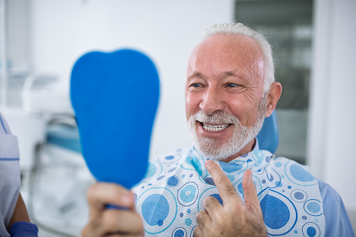 Old man smiling while holding a hand held mirror