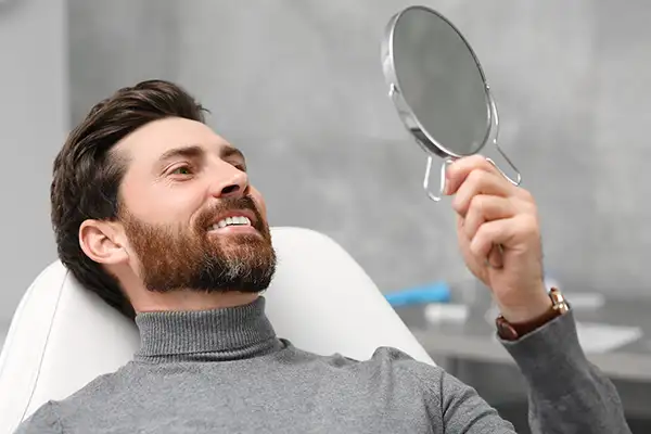 Smiling dental patient leaning back in exam chair and looking up into mirror