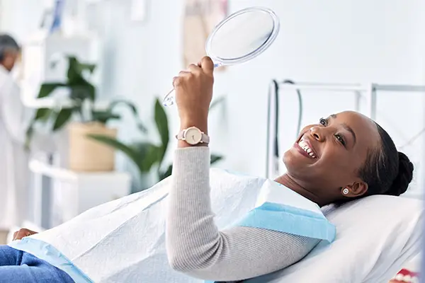 Black woman in dental chair smiling in handheld mirror